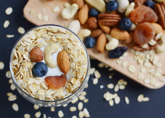 Vitamin breakfast yogurt cocktail with blueberries, oat flakes, dried fruits and nuts in glass. Black background