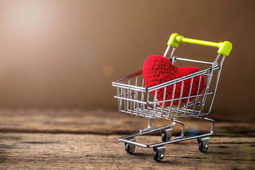 red heart shape in mini shopping cart on wooden mock up background. Image for love shopping concept.