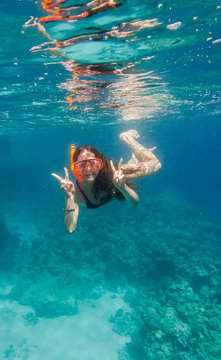 Girl in swimming mask dive underwater near coral reef 