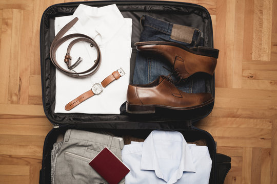 Open traveler's bag with men clothing, accessories, wallet, leather shoes, passport and watch. Travel and vacations concept. 