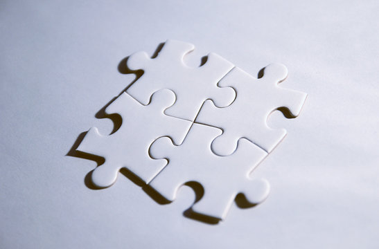 Vier zusammenh&auml;ngende Puzzleteile auf wei&szlig;em Grund