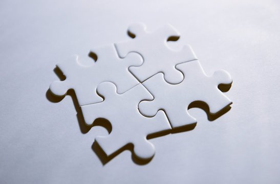 Vier zusammenh&auml;ngende Puzzleteile auf wei&szlig;em Grund