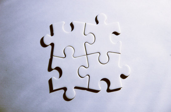 Vier zusammenh&auml;ngende Puzzleteile auf wei&szlig;em Grund
