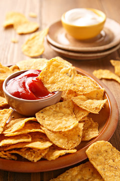 Tortilla chips on a wooden background with red sauce bowl