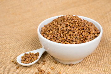 dry buckwheat heap in white bowl with spoon over sackcloth