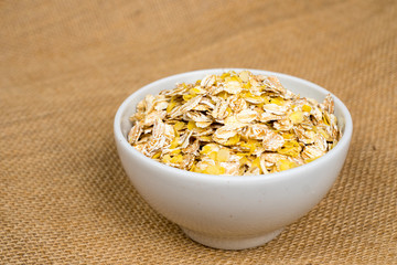 oat flakes heap in white bowl over sackcloth