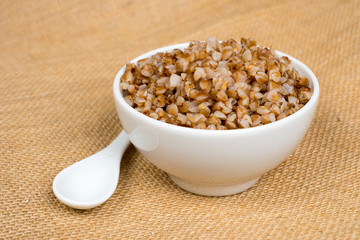 cooked buckwheat heap in white bowl with spoon over sackcloth