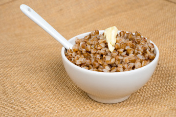 cooked buckwheat heap with butter in white bowl with spoon over sackcloth