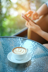 Women playing smart phone with coffee heart latte in hand put on the legs.