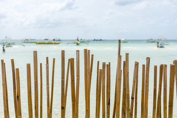 Looking through a bamboo pole barrier fence in a tropical island white sand beach out to a calm...