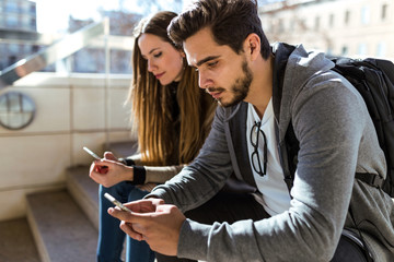 Beautiful young couple using mobile phone in the street.