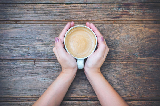 Top view image of woman holding a cup of coffee on wooden vintage table