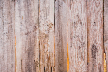 Closeup of texture of old weathered brown wooden fence with sunlight through holes in it. Horizontal color photo.