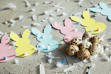 Easter composition of quail eggs with bunny garland and feathers on concrete background. Top view