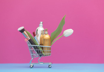 two perfume bottles, brush and white tulip in the shopping cart on the wonderful pink background