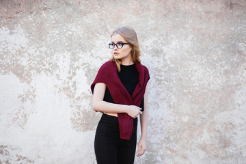Portrait of a young girl with glasses and professional make up standing near a wall