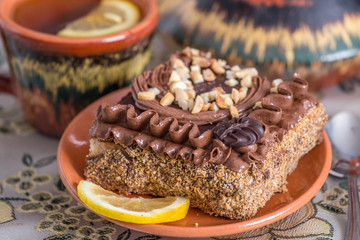 Delicious and sweet chocolate cake with cream and nuts and a сup of black tea with lemon. tea set with teapot, saucer and сup