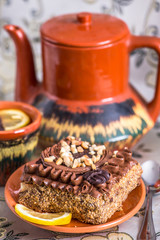 Delicious and sweet chocolate cake with cream and nuts and a сup of black tea with lemon. tea set with teapot, saucer and сup