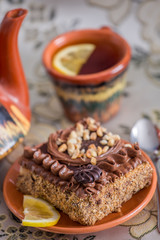 Delicious and sweet chocolate cake with cream and nuts and a сup of black tea with lemon. tea set with teapot, saucer and сup