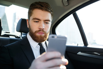 Concentated bearded business man in suit looking at mobile phone in his hand