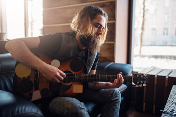Bearded man with guitar sitting on black couch