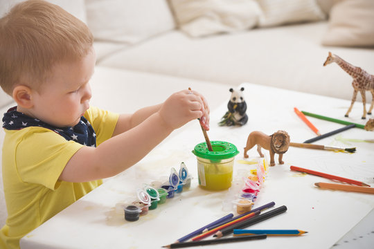 Cute little toddler boy in yellow shirt sitting at table and drawing with colorful paints. indoors. child having fun. Early learning. Creative. Toddler drawing.