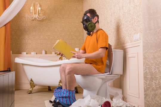 Man in gas mask sitting on toilet and reading book