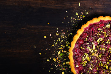 Delicious homamade cranberry, cherry tart with pistachios, powdered sugar on dark wooden background...