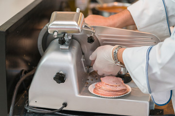 chef wearing rubber glove  using ham slicer machine