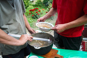 man pours a fish soup from a bowler into a bowl , fish soup cooked at the stake, fish soup cooking...