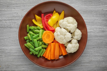 Bowl with fresh vegetables on wooden background