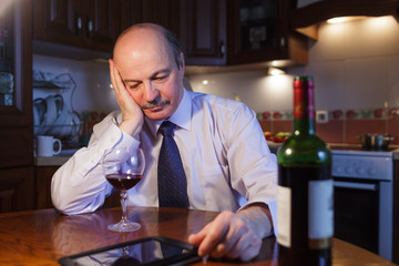 Tired businessman in white shirt and tie is drinking red wine in the kitchen after work