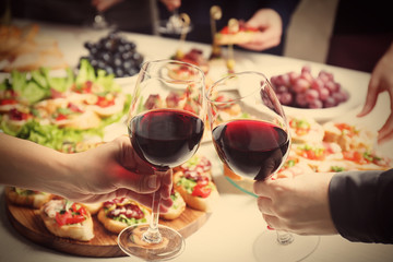 People clinking glasses with wine and delicious dishes on table