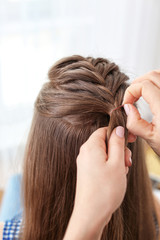 Fototapeta premium Hairdresser making braid hairstyle to young beautiful woman, closeup