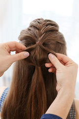 Fototapeta premium Hairdresser making braid hairstyle to young beautiful woman, closeup