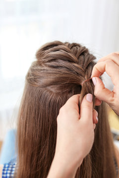 Hairdresser making braid hairstyle to young beautiful woman, closeup