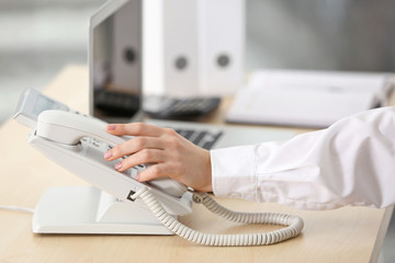 Female hand picking up telephone receiver in office
