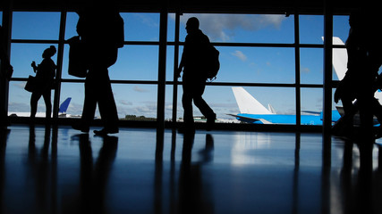 Fototapeta na wymiar Travellers with suitcases and baggage in airport walking to departures in front of window, silhouette