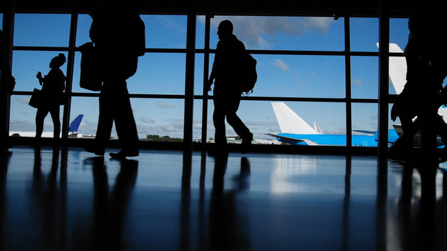 Travellers with suitcases and baggage in airport walking to departures in front of window, silhouette