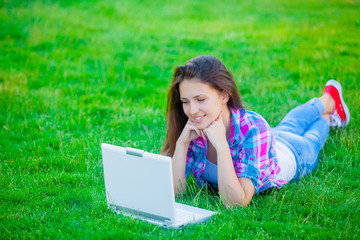 beautiful young girl lying on the field with laptop on the wonderful grass background