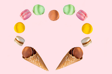 Multicolored cake macaron or macaroons and waffle cones in the form of a heart frame on the pink background. Top view. Free space for text