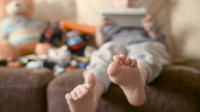Barefoot boy sitting on the bed and play games