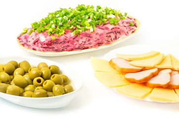 Green olives sliced cheese and salami in a saucer on a white background
