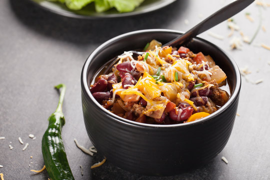 Kidney Bean Chili with tomato chunks and onion topped with cheese in large black bowl horizontal shot