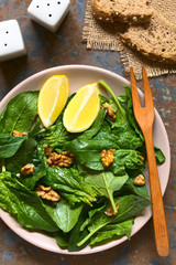 Fresh spinach and walnut salad with lemon wedges on the side served on plate, photographed overhead on slate with natural light