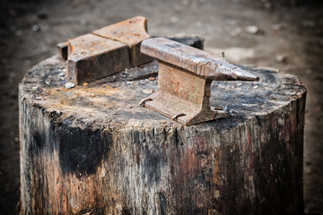 Old big anvils on the stump. Tool blacksmith, located on a huge tree stump. And 
tools for beat scythe grass.