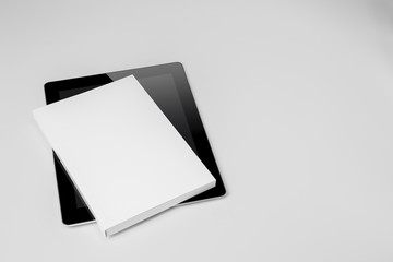Real paperback white book over a tablet on a gray background