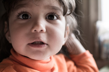 Child girl sitting at a table and gesturing with his hands.
