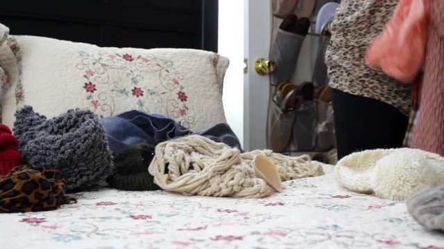 Woman hanging up scarves from clothing pile on bed
