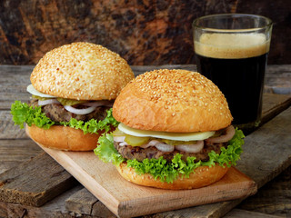 veggie burgers with a chop of black beans, lettuce, pickled onions, cucumber and a glass of dark beer on a wooden background.